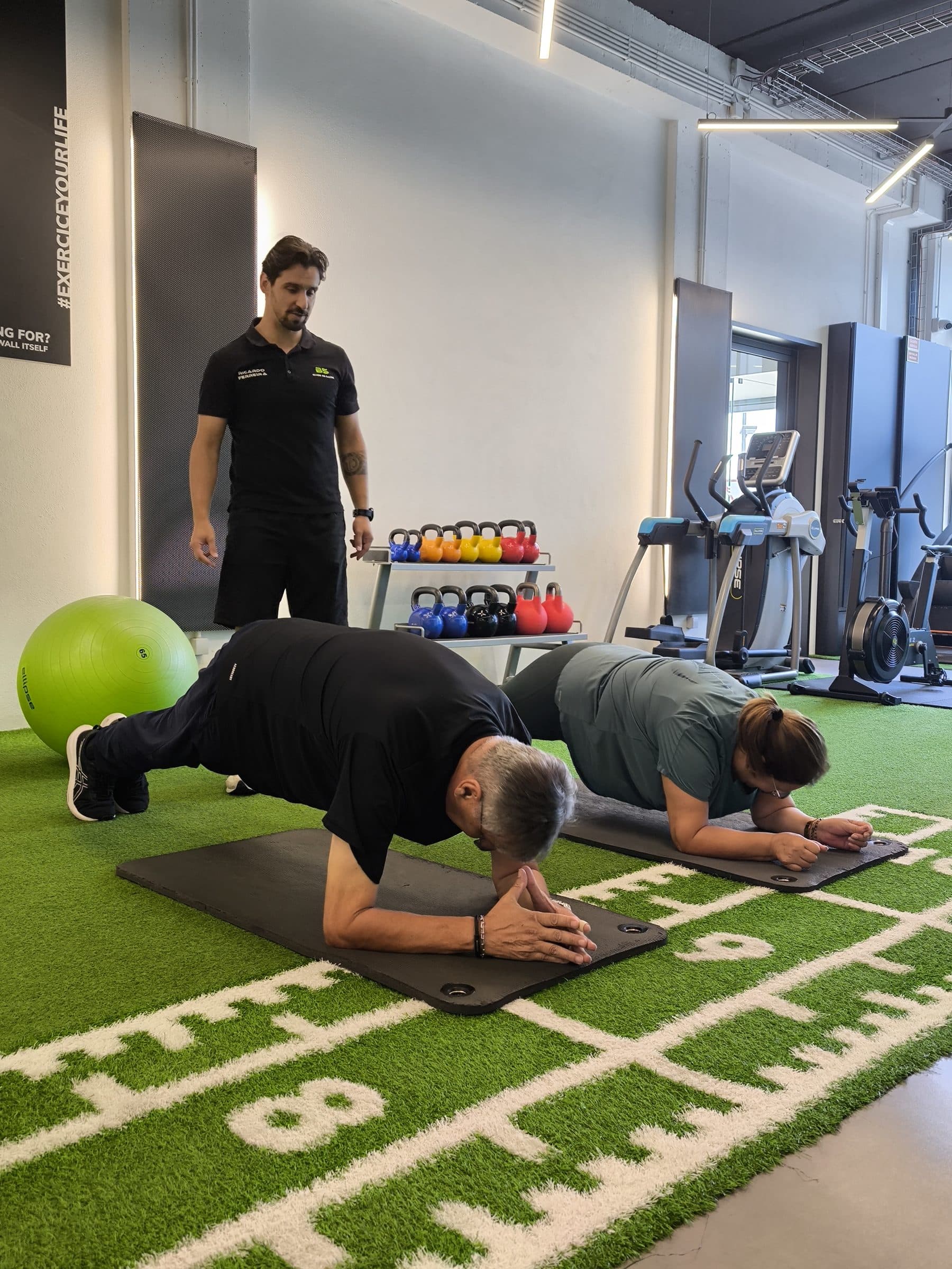 Sessão de treino personalizado no BSPLACE: duas pessoas em prancha, com o profissional a acompanhar